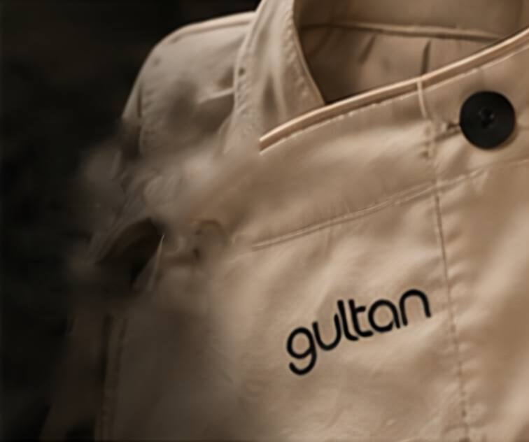 Close crop of a cream chef jacket collar with an embroidered Gultan wordmark.