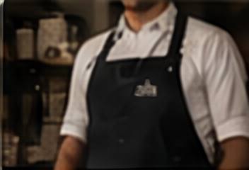 A server in a white shirt and dark apron embroidered with a restaurant wordmark.